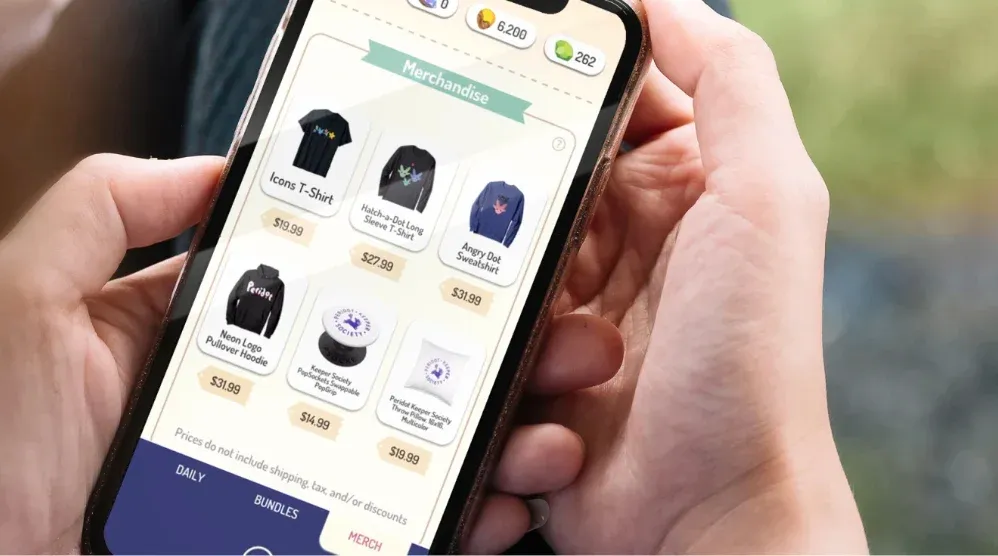 A person holding a smartphone with an app open showing merchandise like T-shirts, hoodies, and pillows available for purchase.