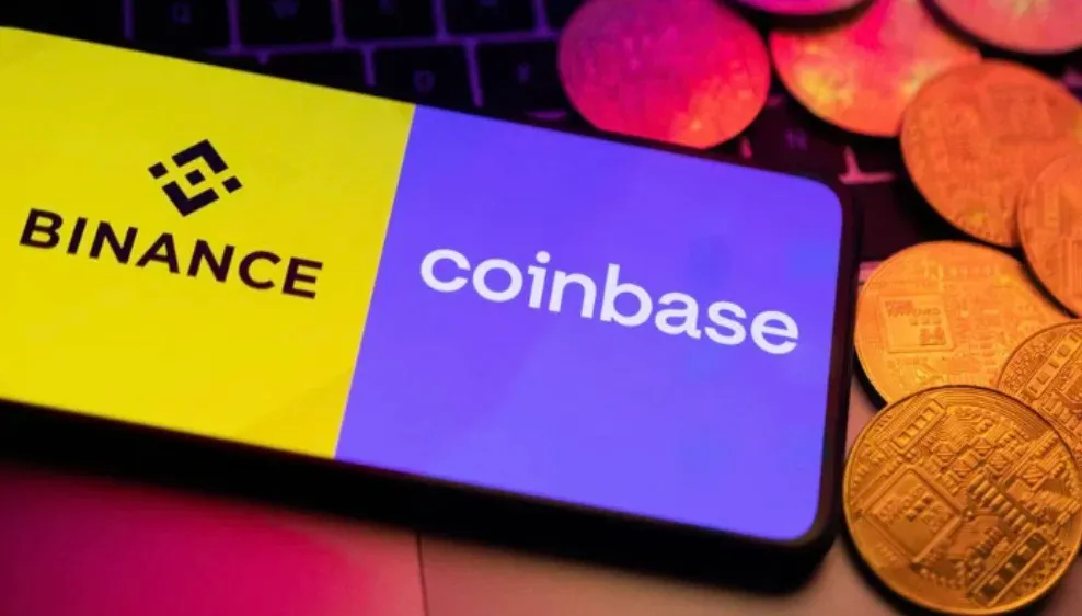 A smartphone screen displaying the logos of Binance and Coinbase, placed on a keyboard with several gold-colored coins around it.